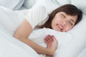 Image of a young female lying in bed suffering from teeth grinding, also known as Bruxism, Charlotte, NC